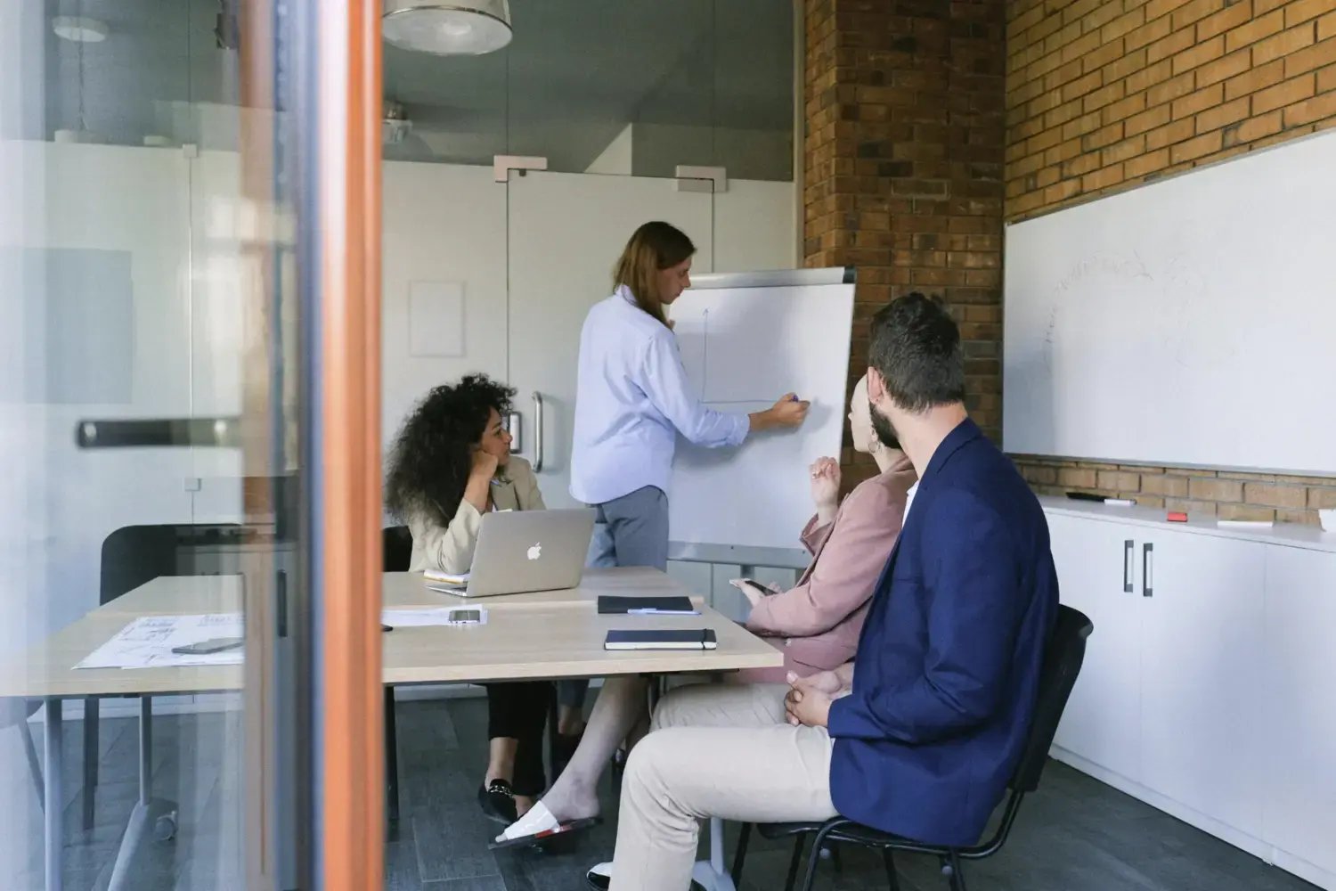 Business team discussing a challenge, with a woman writing notes on a whiteboard in a modern office Business team discussing a challenge, with a woman writing notes on a whiteboard in a modern office